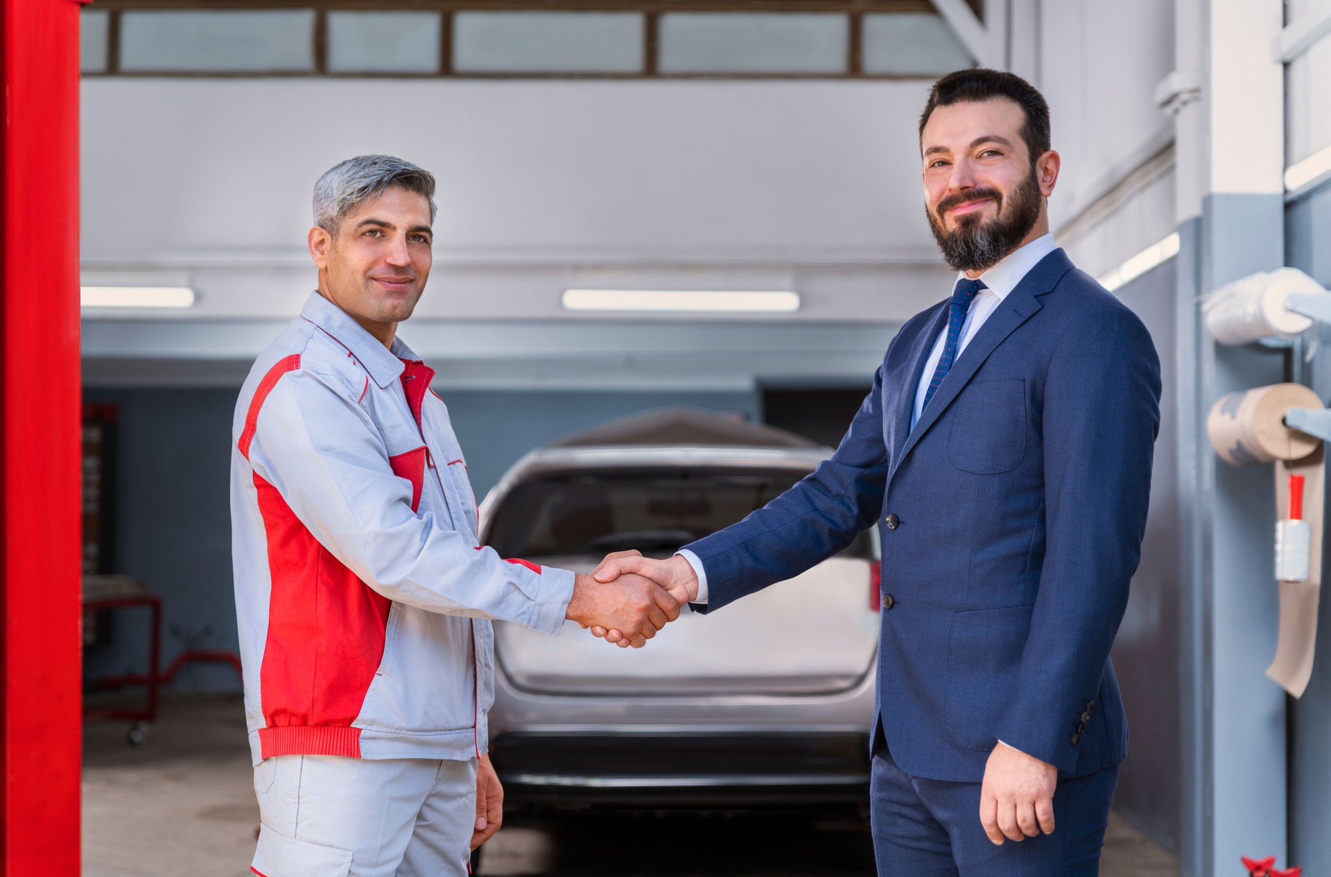 Reparador de coches es apretón de manos para mirar la cámara con el hombre de negocios en el taller de reparación de automóviles